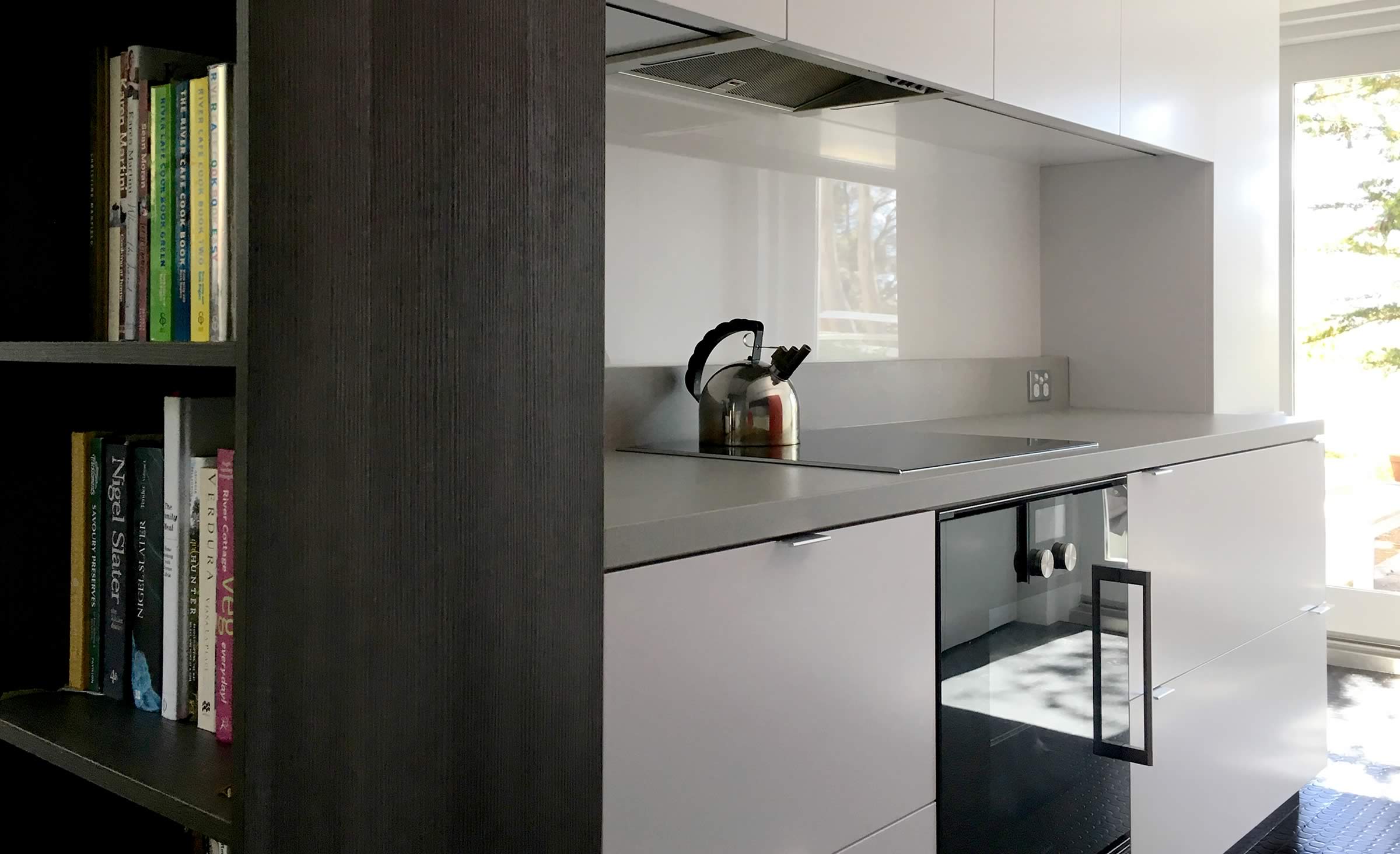 Customised kitchen joinery incorporating bookcase, stone tops, flush installed oven, and soft close cupboards.
